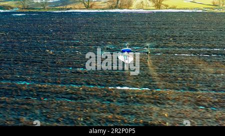 Argodrone laisse tomber de l'engrais sur les champs par le dessus. Terre noire et neige. Les agriculteurs se préparent à semer le blé, le maïs, le colza et les céréales. Engrais f Banque D'Images