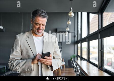 Un homme d'affaires de milieu d'âge heureux tenant un téléphone portable au bureau. Banque D'Images