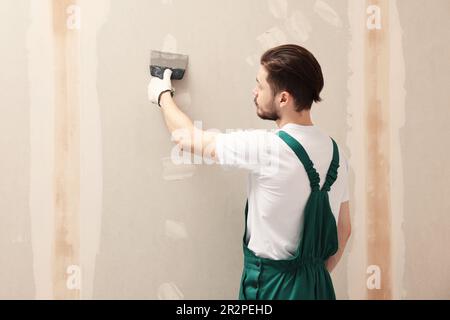 Travailleur dans un mur uniforme de plâtrage avec couteau à mastiquer à l'intérieur Banque D'Images