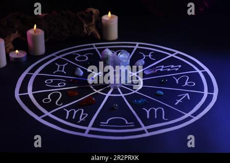 Pierres naturelles pour les signes du zodiaque, carte d'astrologie dessinée et bougies allumées sur table bleu foncé Banque D'Images