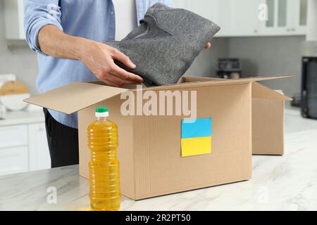 Aide humanitaire pour l'Ukraine. Homme mettant des vêtements dans une boîte de dons à la table blanche à l'intérieur, gros plan Banque D'Images