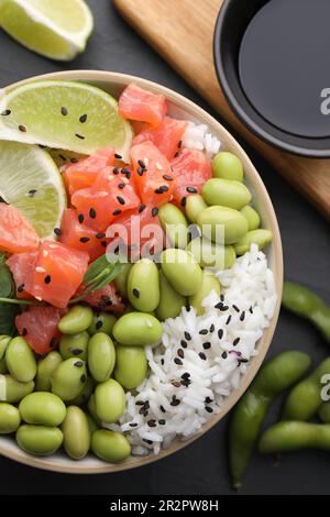 Délicieux poke Bowl avec citron vert, poisson et haricots édamames sur table noire, plat Banque D'Images