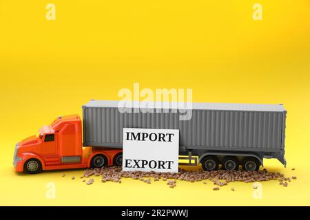 Carte avec mots Import and Export, grains de blé près d'un camion de jouets sur fond jaune Banque D'Images