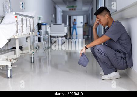 Un médecin asiatique fatigué portant des exfoliants assis dans un couloir à l'hôpital Banque D'Images