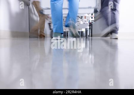 Bas de la section de divers médecins poussant le patient dans le lit d'hôpital dans le couloir, flou de mouvement Banque D'Images