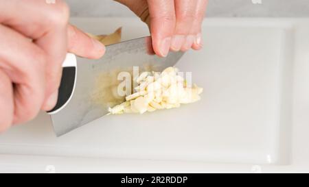 Une femme hache de l'ail frais à l'aide d'un couteau de cuisine, vue rapprochée Banque D'Images