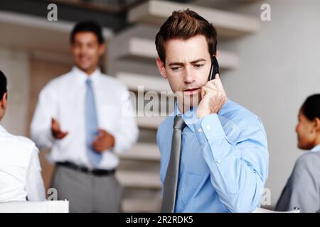 Prendre un appel important pendant une présentation. Un jeune cadre prenant un appel pendant une présentation d'affaires. Banque D'Images