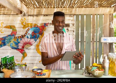Portrait d'un barman afro-américain tenant une tablette dans un bar de plage, sans modification Banque D'Images