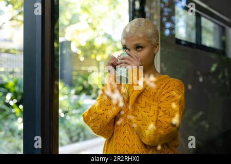 Bonne femme biraciale à la mode et non modifiée buvant du café à la maison, en regardant par la fenêtre. Détente, temps libre et style de vie domestique. Banque D'Images