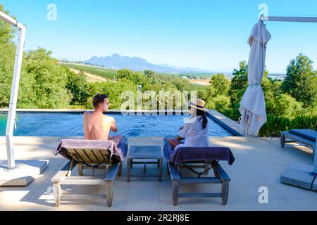 Couple d'hommes et de femmes se détendant dans une piscine avec vue sur un paysage de vignoble au coucher du soleil avec des montagnes à Stellenbosch, près du Cap, Afrique du Sud. Banque D'Images