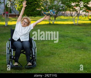 Femme caucasienne âgée faisant des exercices en étant assise dans un fauteuil roulant à l'extérieur. Banque D'Images