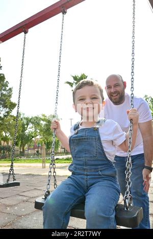 Joyeux père pousse des balançoires avec son petit fils mignon. Une famille heureuse passe du temps ensemble dans le parc, jour d'été ensoleillé Banque D'Images