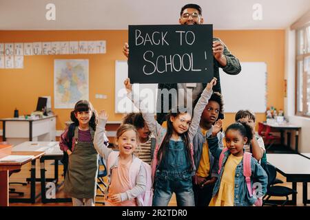 Enseignant et élèves tenant un panneau de retour à l'école dans une salle de classe. La classe de l'école élémentaire est heureuse de retourner à l'école et d'entrer dans une nouvelle année. BA Banque D'Images