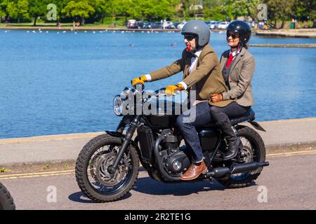 Poole, Dorset Royaume-Uni. 21 mai 2023 Bournemouth et Poole Distinguished Gentlemen’s Ride est un événement annuel, l’un des nombreux dans le monde, qui vise à recueillir des fonds et à sensibiliser la population à la santé des hommes. Dans le cadre de leur balade, des centaines de motos, beaucoup vintage, traversent Poole Park sur leur chemin vers Bournemouth avec beaucoup de leurs coureurs habillés de manière appropriée, dans des cravates de style rétro, des moustaches et des tweeds par une belle journée ensoleillée. Homme avec passager de passager de passager de passager de passager vêtu en veste, gilet de costume et cravate chevauchant Triumph moto, homme avec pipe dans la bouche crédit : Carolyn Jenkins / Alamy Live News Banque D'Images