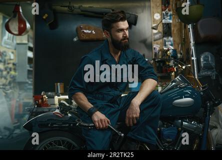 Portrait d'un homme confiant en combinaison tenant la clé en position assise sur la moto Banque D'Images