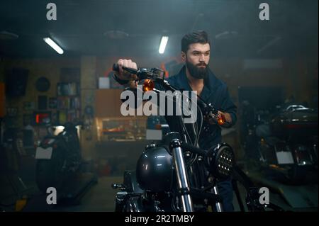 Un mécanicien automobile déplace la moto sur un banc de réparation dans un garage d'atelier Banque D'Images
