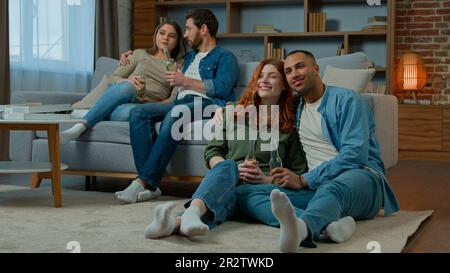 Quatre amis ethniques différents regardent la télévision dans un home cinéma spectateurs regardant la chaîne Smart tv comédie show série film multiracial Banque D'Images