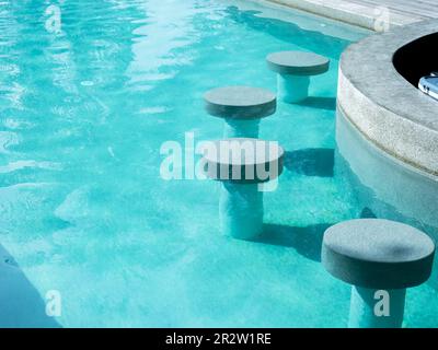 Des tabourets de bar ronds et vides en terrazzo s'asseoir dans une piscine d'eau claire et propre pour préparer les clients à la station le jour ensoleillé. Extérieur du bar de la piscine Banque D'Images