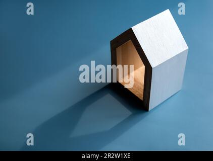 Maison, maison, famille, immobilier, investissement immobilier. Petite maison en bois miniature blanc minimaliste isolée sur fond bleu foncé avec lumière Banque D'Images