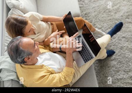 Retraite et technologies modernes. Vue ci-dessus des conjoints âgés assis sur un canapé avec un ordinateur portable et une tablette numérique, maquette Banque D'Images