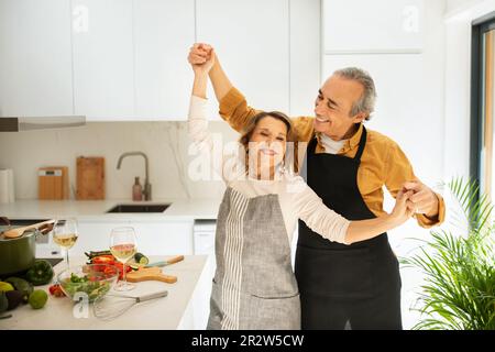 Amoureux couple senior dansant tout en cuisinant ensemble dans la cuisine, heureux mari appréciant le temps avec sa belle femme Banque D'Images