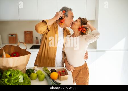 Les conjoints âgés amoureux arrivant du supermarché avec sac d'épicerie et de déballage, s'amuser et s'embrasser dans la cuisine Banque D'Images