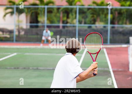 Garçon jouant au tennis sur un court extérieur. Adolescent avec raquette de tennis et ballon dans le club de sport. Exercice actif pour les enfants. Activités estivales pour les enfants. Banque D'Images