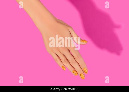 Des mains de femmes soignées avec un motif à ongles tendance sur fond rose Banque D'Images