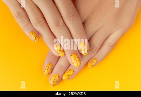 Des mains de femmes soignées avec un motif à ongles tendance sur fond orange Banque D'Images