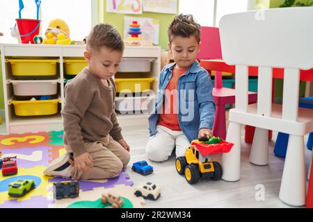 Adorables garçons jouant avec des voitures jouet et tracteur assis sur le sol à la maternelle Banque D'Images