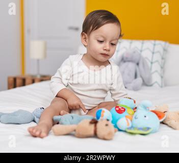 Adorable garçon hispanique assis sur le lit avec des poupées dans la chambre Banque D'Images