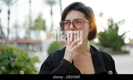 Jeune femme caucasienne portant des lunettes de soleil fumant au parc Banque D'Images