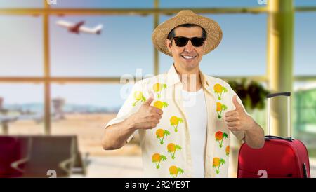 Latin homme en vacances portant une chemise à fleurs chapeau lunettes de soleil à l'aéroport faisant des pouces heureux vers le haut geste avec les mains. Approbation de l'expression en regardant la came Banque D'Images