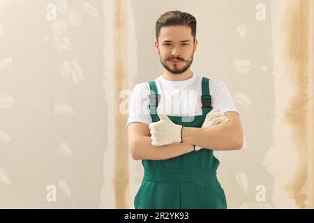 Un bon ouvrier en uniforme près du mur avec du mastic à l'intérieur. Espace pour le texte Banque D'Images