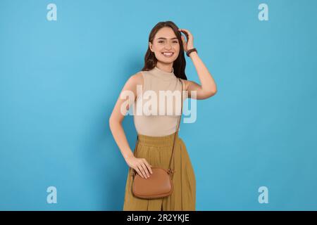 Belle jeune femme avec une tenue tendance et un sac élégant sur fond bleu clair Banque D'Images