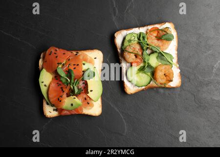 Toasts savoureux avec différentes garnitures sur table noire, plat Banque D'Images