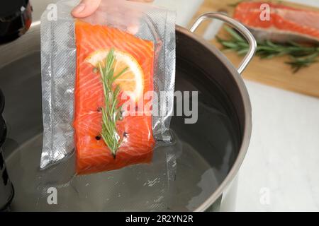 Femme mettant le saumon emballé sous vide dans une casserole avec cuisinière sous vide dans la cuisine, gros plan. Circulateur à immersion thermique Banque D'Images