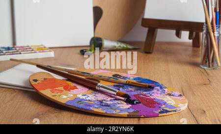 Palette de l'artiste avec des peintures et des pinceaux mélangés sur une table en bois Banque D'Images