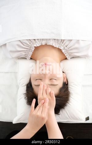 Femme recevant une acupression entre les yeux dans une clinique d'acupuncture Banque D'Images