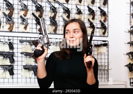 Une femme joyeuse imitant de viser avec deux pistolets dans un magasin d'armes à feu Banque D'Images