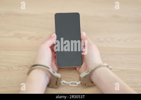 Une femme aux menottes tient un téléphone portable moderne assis au bureau Banque D'Images
