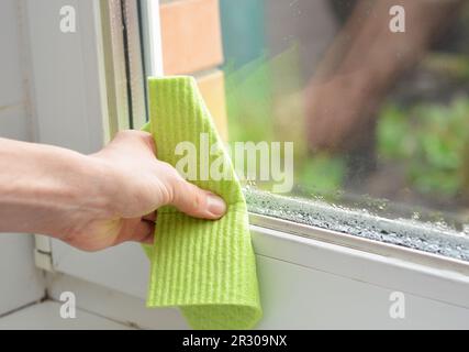 Femme essuie la main pour éliminer la condensation d'eau dans la pièce avec un taux d'humidité élevé. Humidité de la maison avec condensation d'eau sur la vitre de fenêtre. Banque D'Images