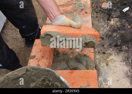 Mason posant le mur de brique de maison avec mortier sur le côté de la brique. Banque D'Images