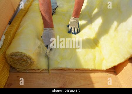 Entrepreneur de couvreur isolant le toit de la maison et coupant la laine minérale avec un couteau. Isolation de la maison pendant la construction de la toiture. Banque D'Images