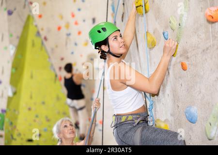 Jeune femme bien équipée, bonne formation sur mur de pierre, montagne artificielle avec rochers, escalade dans le parc de rochers à l'intérieur Banque D'Images