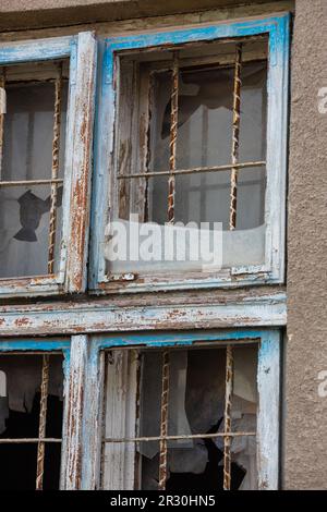 Vieille fenêtre avec des volets en bois usés et du verre cassé sur le mur extérieur d'une ancienne maison en ruines. Banque D'Images