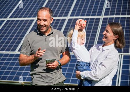 Famille moderne investissant dans leur fils. L'homme, sa femme et son petit fils sont heureux de l'argent qu'ils ont économisé en achetant des panneaux solaires. Concept d'économie d'argent, d'investissement dans les énergies renouvelables. Banque D'Images