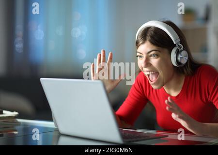 Une femme excitée regardant des médias sur un ordinateur portable et un casque dans la nuit à la maison Banque D'Images