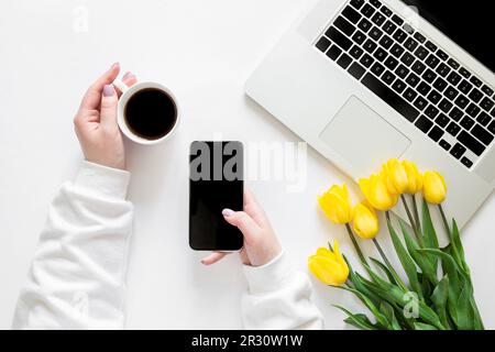 Smartphone et une tasse de café entre les mains des femmes sur fond blanc, vue du dessus. Banque D'Images