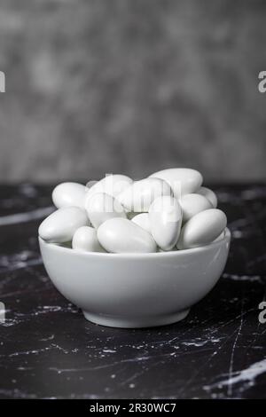 Chocolat et dragee aux amandes. Dragee au chocolat dans un bol en céramique sur fond sombre Banque D'Images